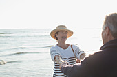 Mature couple holding hands on sunny ocean beach