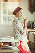 Pensive mature woman drinking wine in kitchen