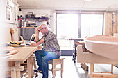 Male carpenter working at laptop near wood boat