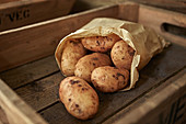 Rustic fresh dirty potatoes in bag in wooden crate
