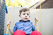 Portrait serious preschool boy swinging on swing