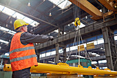 Male worker guiding hydraulic crane in factory