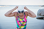 Female swimmer adjusting swimming goggles at ocean