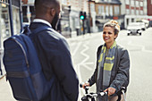 Friends with bicycle talking on sunny urban street