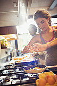 Young woman cracking egg over skillet on stove