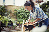 Young woman measuring and marking wood on patio