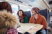 Smiling young friends planning with map on train