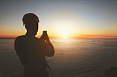 Silhouette rock climber photographing sunset