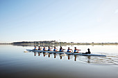 Female rowing team rowing scull on tranquil lake