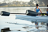 Female rower with oar rowing scull on lake