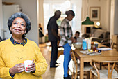 Senior woman drinking coffee with family in background