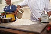 Close up chef pouring water into pizza dough flour nest