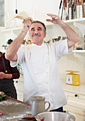 Playful senior chef tossing pizza dough in kitchen