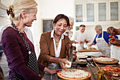 Senior women friends grating cheese over pizza