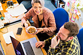 Business people eating cereal, working at laptop on office