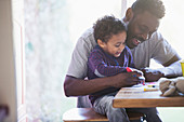 Happy father and toddler son colouring at table