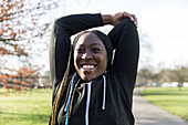 Portrait female runner stretching arms in park