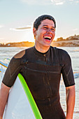 Laughing male surfer with surfboard on beach