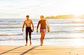 Male surfers carrying surfboards on ocean beach