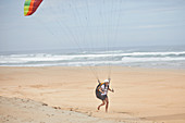 Male paraglider running on ocean beach