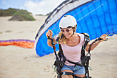 Smiling female paraglider with parachute on beach