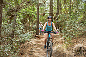 Carefree woman mountain biking on trail in woods