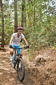 Mature man mountain biking on trail in woods