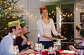 Woman in paper crown serving Christmas pudding