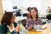 Happy businesswomen eating lunch in office