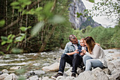 Parents and baby son sitting on rocks along stream