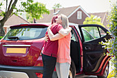 Lesbian couple hugging by car in sunny driveway