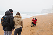 Woman photographing husband and daughter on beach