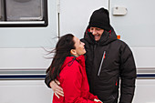 Couple in warm clothing hugging outside motor home
