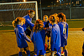 Soccer coach and girls soccer team in huddle