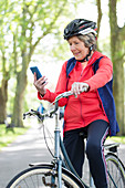 Active senior woman using smart phone on bike