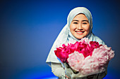 Young woman in hijab holding pink peonies