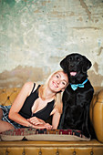 Young woman with black dog wearing bow tie on sofa