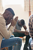 Serene man praying with rosary in prayer group