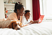 Mother and son using digital tablet on bed next to dog