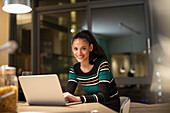 Portrait smiling woman using laptop in apartment at night