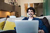 Portrait smiling man using laptop on apartment sofa