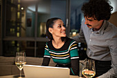 Couple using laptop and drinking white wine