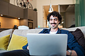 Smiling man using laptop on apartment sofa