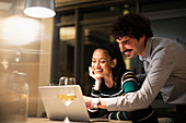 Happy couple using laptop and drinking white wine
