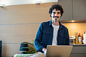 Portrait smiling man using laptop in apartment kitchen