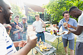 Male friends laughing and eating around barbecue grill