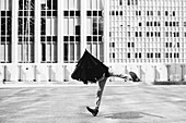 Man dancing with umbrella on head outside urban buildings