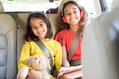 Portrait sisters with teddy bear riding in back seat of car