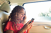 Smiling tween girl using smart phone in back seat of car