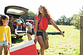 Sisters camping, carrying cooler in field